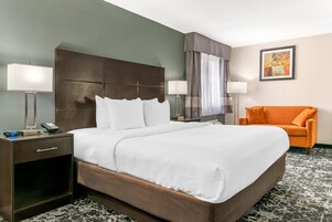 Habitación de hotel con una cama grande, dos mesitas de noche, una lámpara, un sillón naranja, un cuadro en la pared y una alfombra estampada.