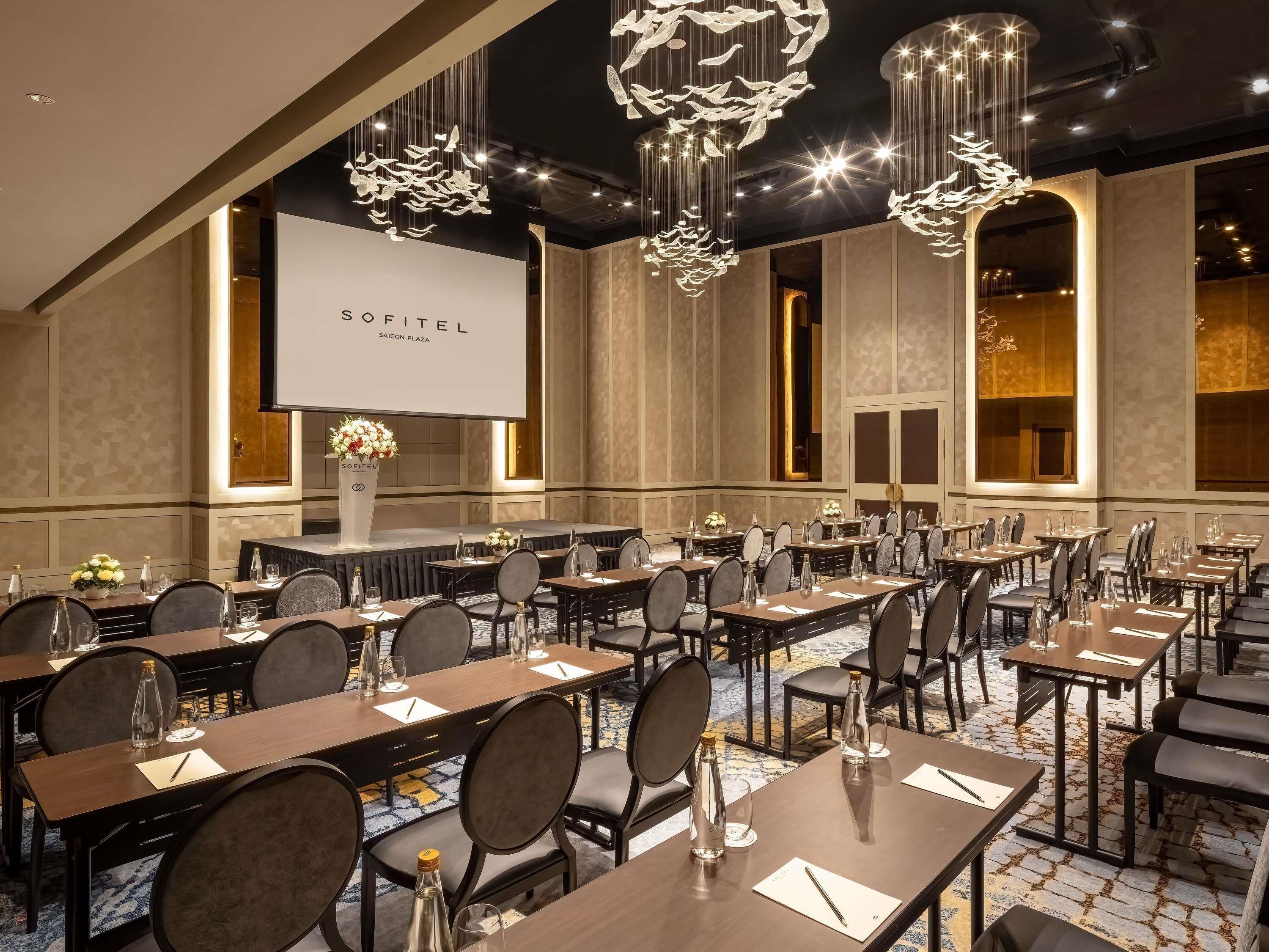Une salle de conférence équipée de tables, de chaises et d’un grand écran affichant le texte « SOFITEL SAIGON PLAZA ».
