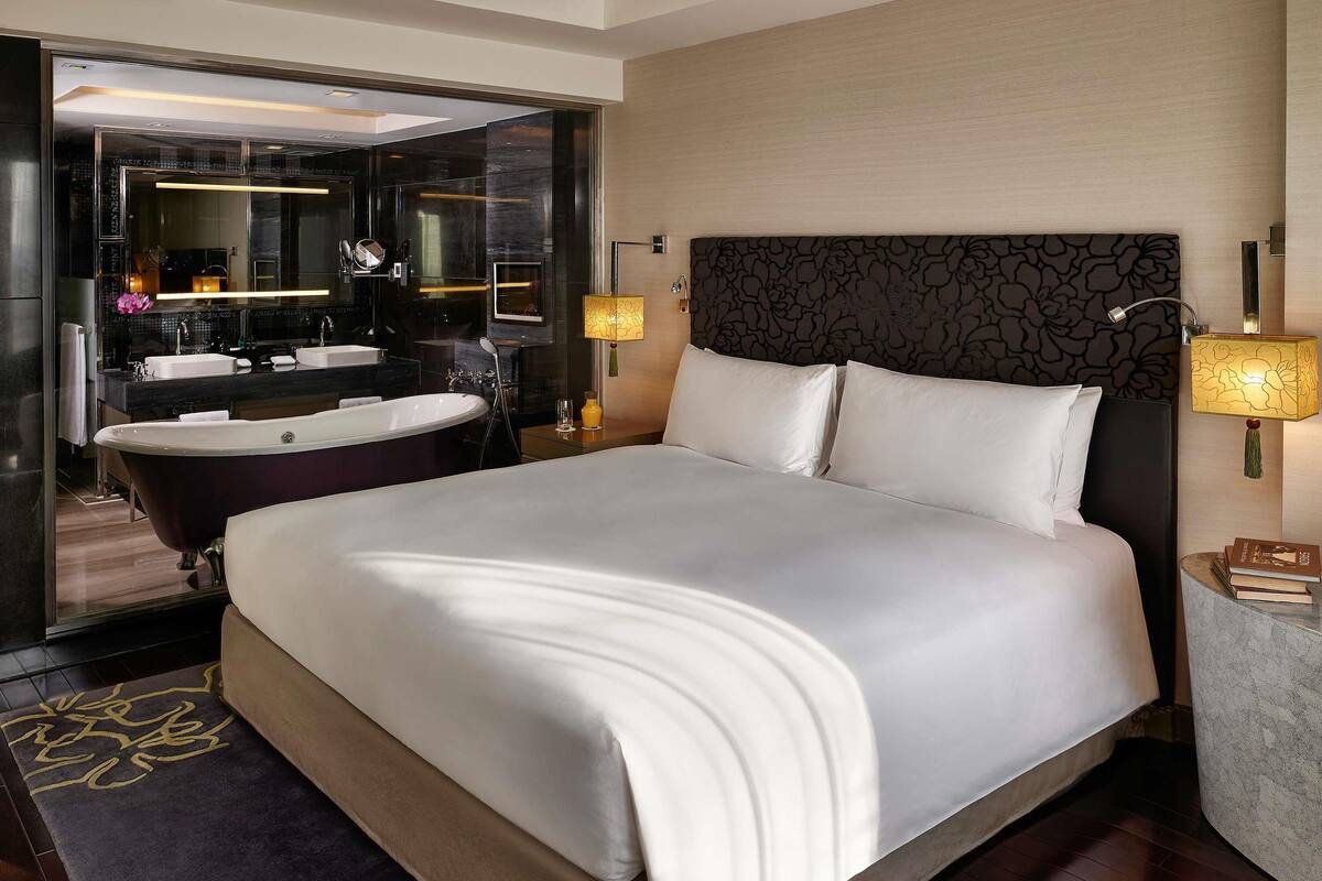Une chambre d’hôtel moderne dotée d’un grand lit, d’une salle de bain séparée avec une baignoire et d’un grand miroir.