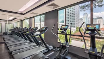 Une salle de sport équipée de tapis de course et d’appareils elliptiques, de grandes fenêtres offrant une vue sur la ville et un aménagement intérieur moderne.