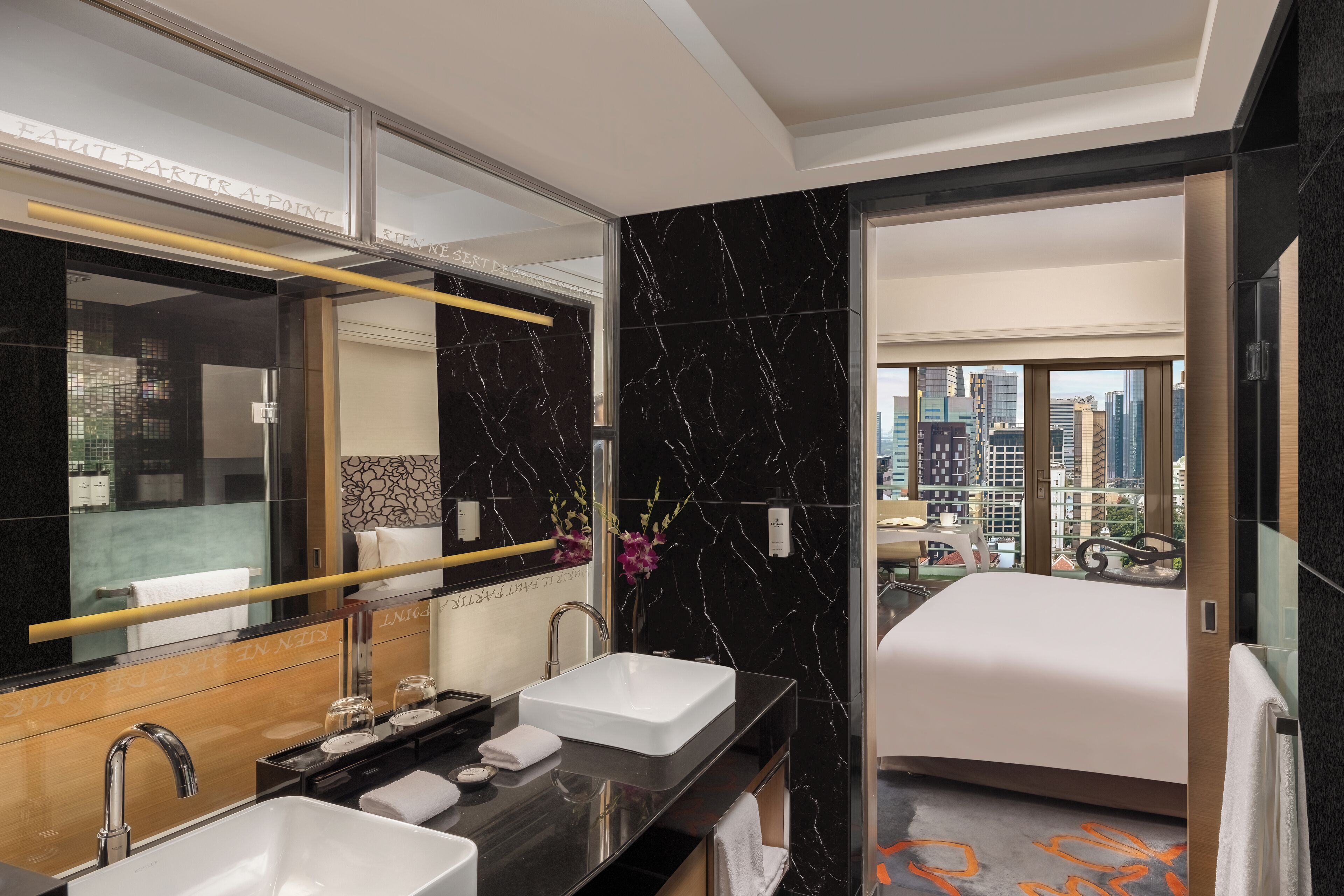 A modern hotel bathroom with dual sinks, a large mirror, and a view of the cityscape through the door.