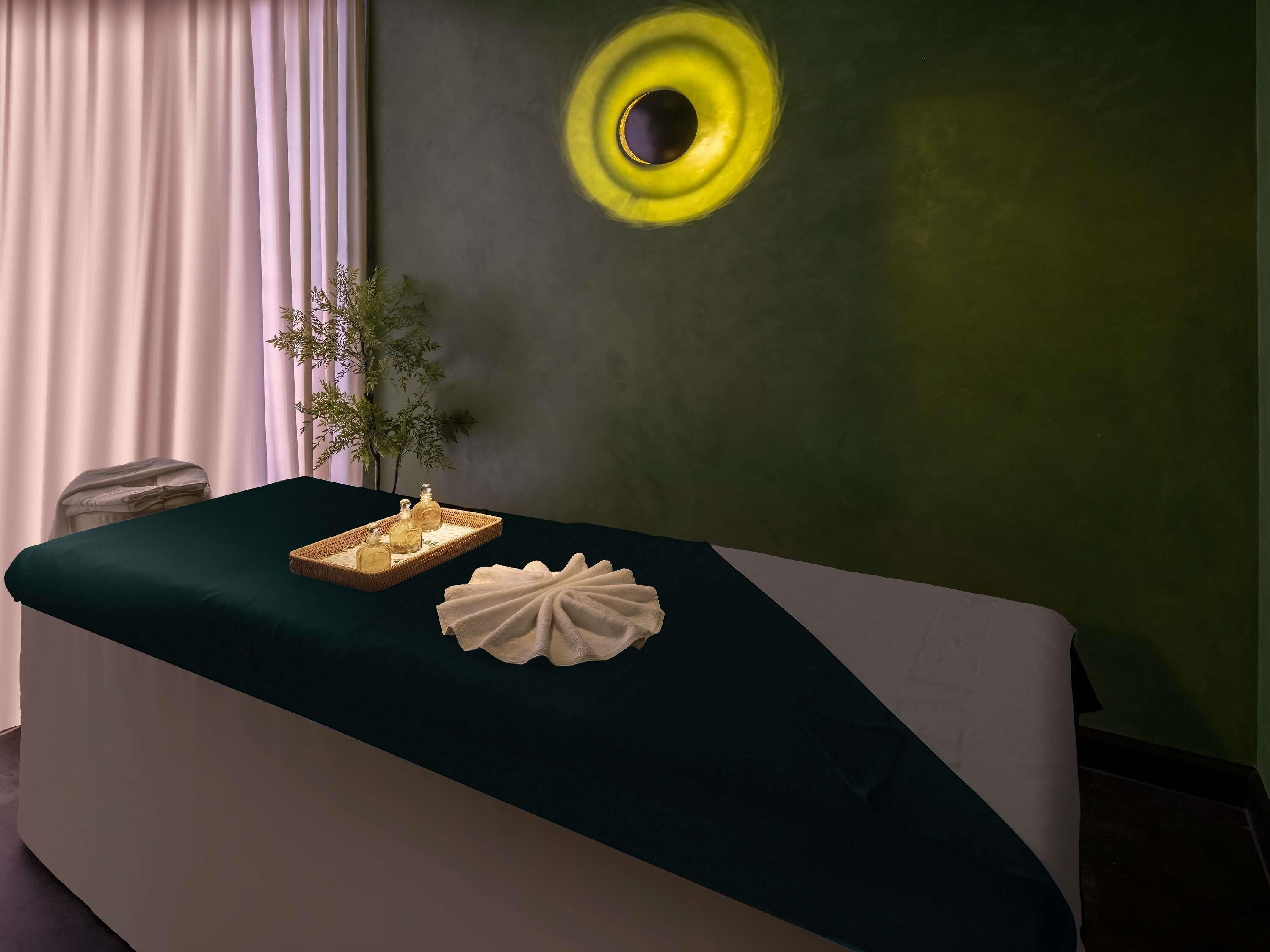 A room with a dark green sofa, a tray with bottles, a decorative white object, and a circular light on the wall.