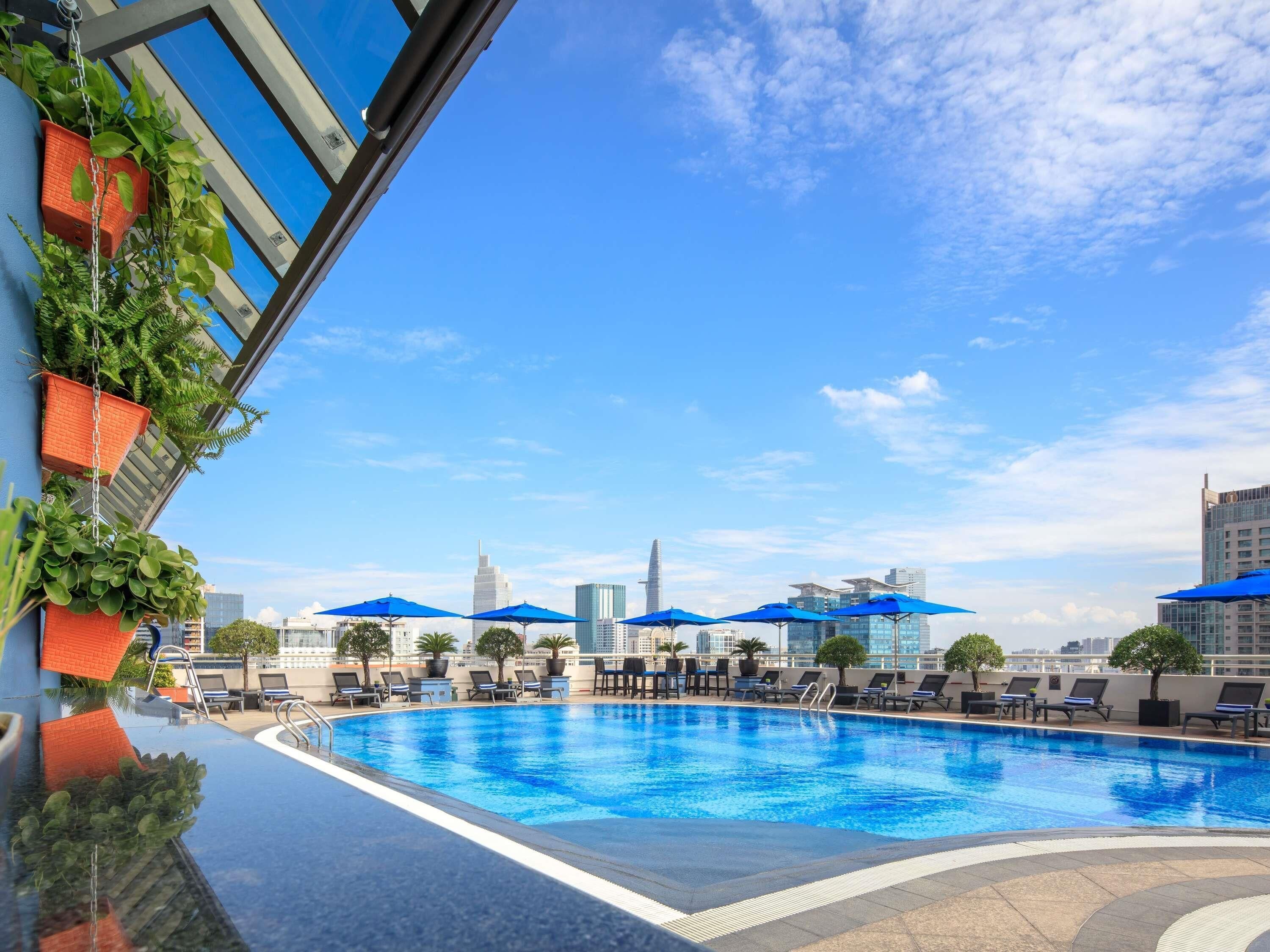 A rooftop pool with blue umbrellas, lounge chairs, and a city skyline in the background.