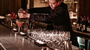 A bartender pouring a drink into a martini glass at a bar.