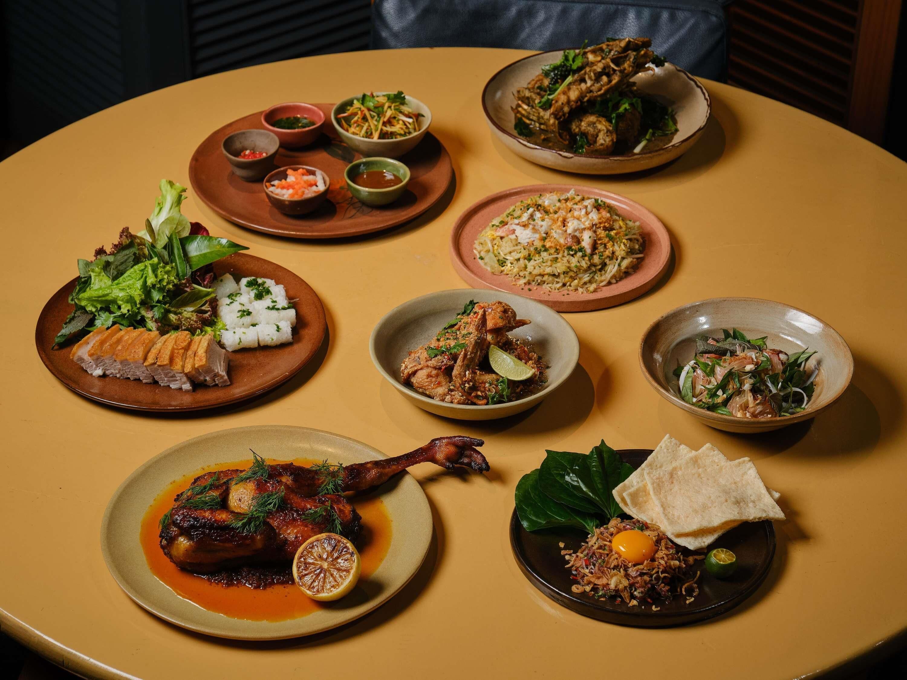 Een ronde tafel met diverse gerechten, waaronder een gebraden eendenpoot, rijstgerechten en een salade.