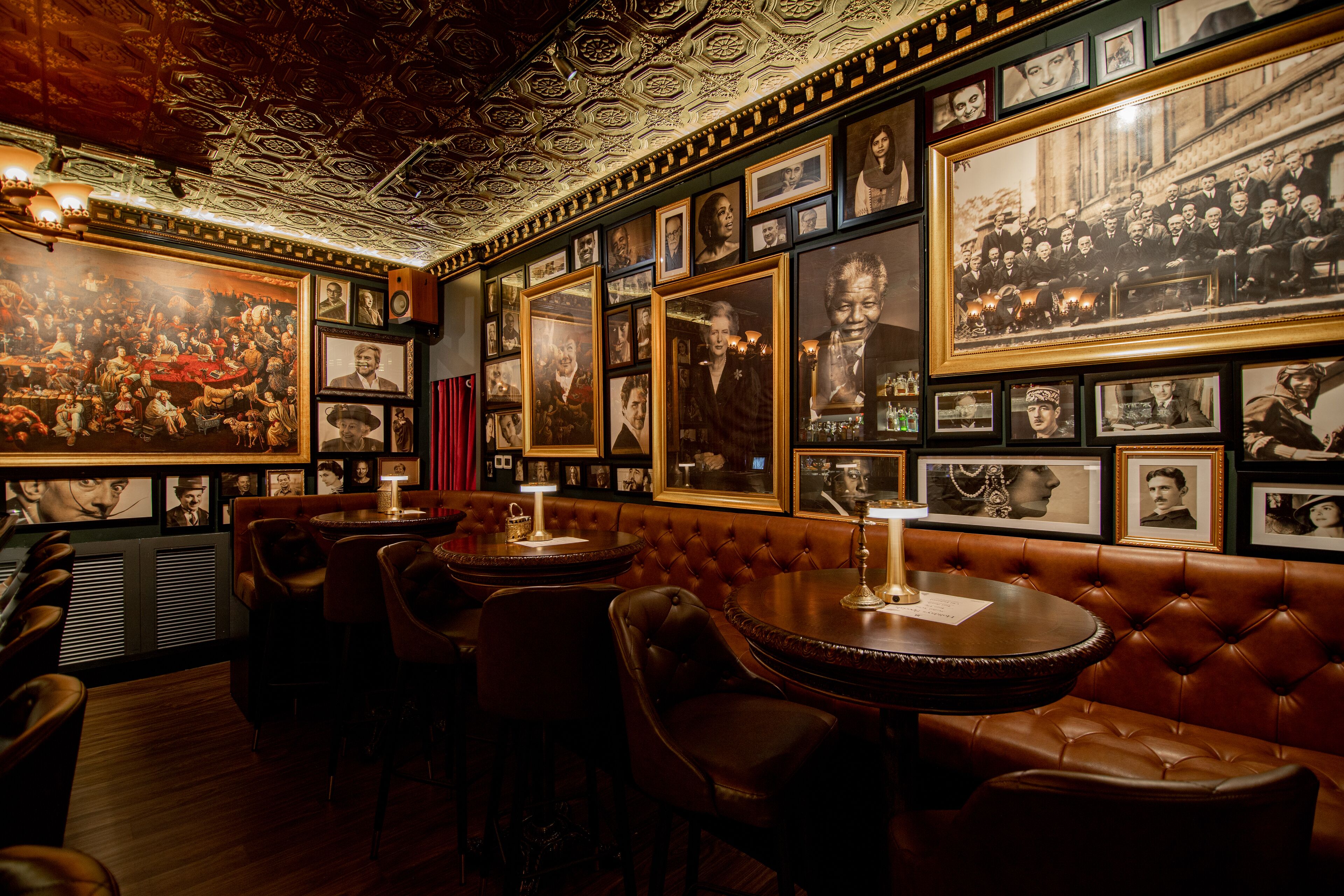 A bar area with leather booths, framed photographs on the walls, and a patterned ceiling.