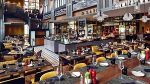 A spacious restaurant with multiple dining areas, a bar, and a staircase leading to an upper level.