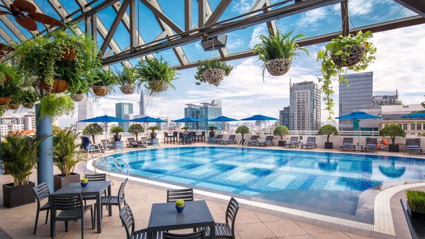 A rooftop pool area with hanging planters, lounge chairs, and a city skyline view.