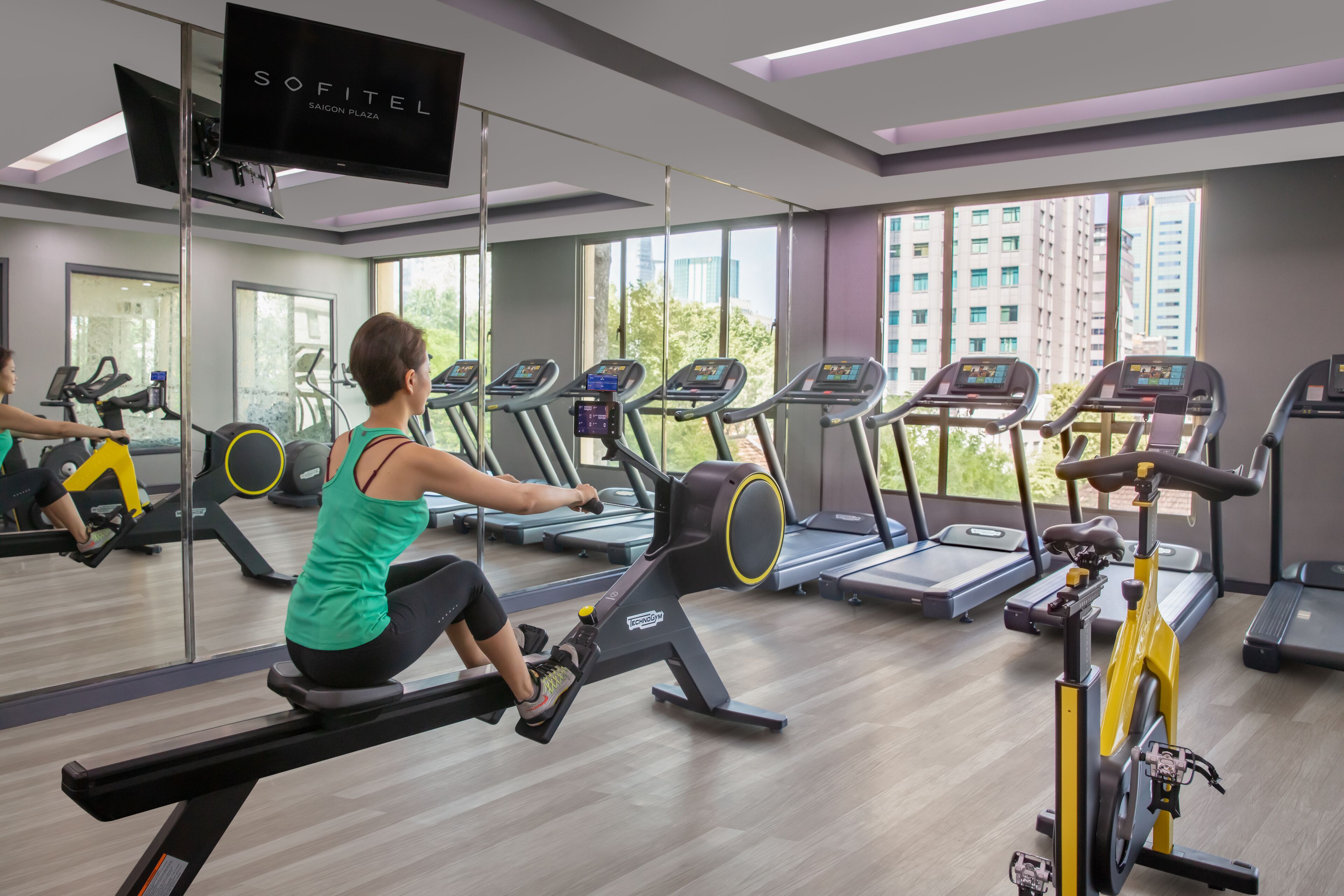 Un gimnasio con máquinas de remo, cintas de correr y una pantalla de televisión mostrando 