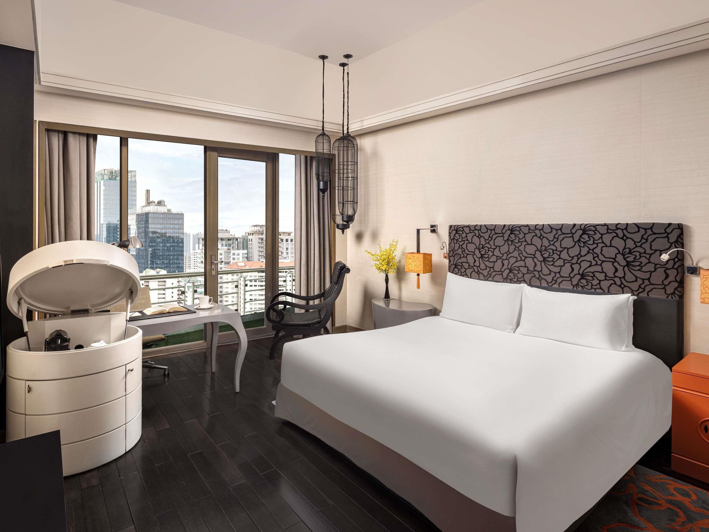 Habitación de hotel con una cama grande, un escritorio, una silla, una lámpara y vistas a la ciudad.