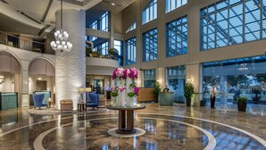 A spacious lobby with a central round table, large windows, and a high ceiling.