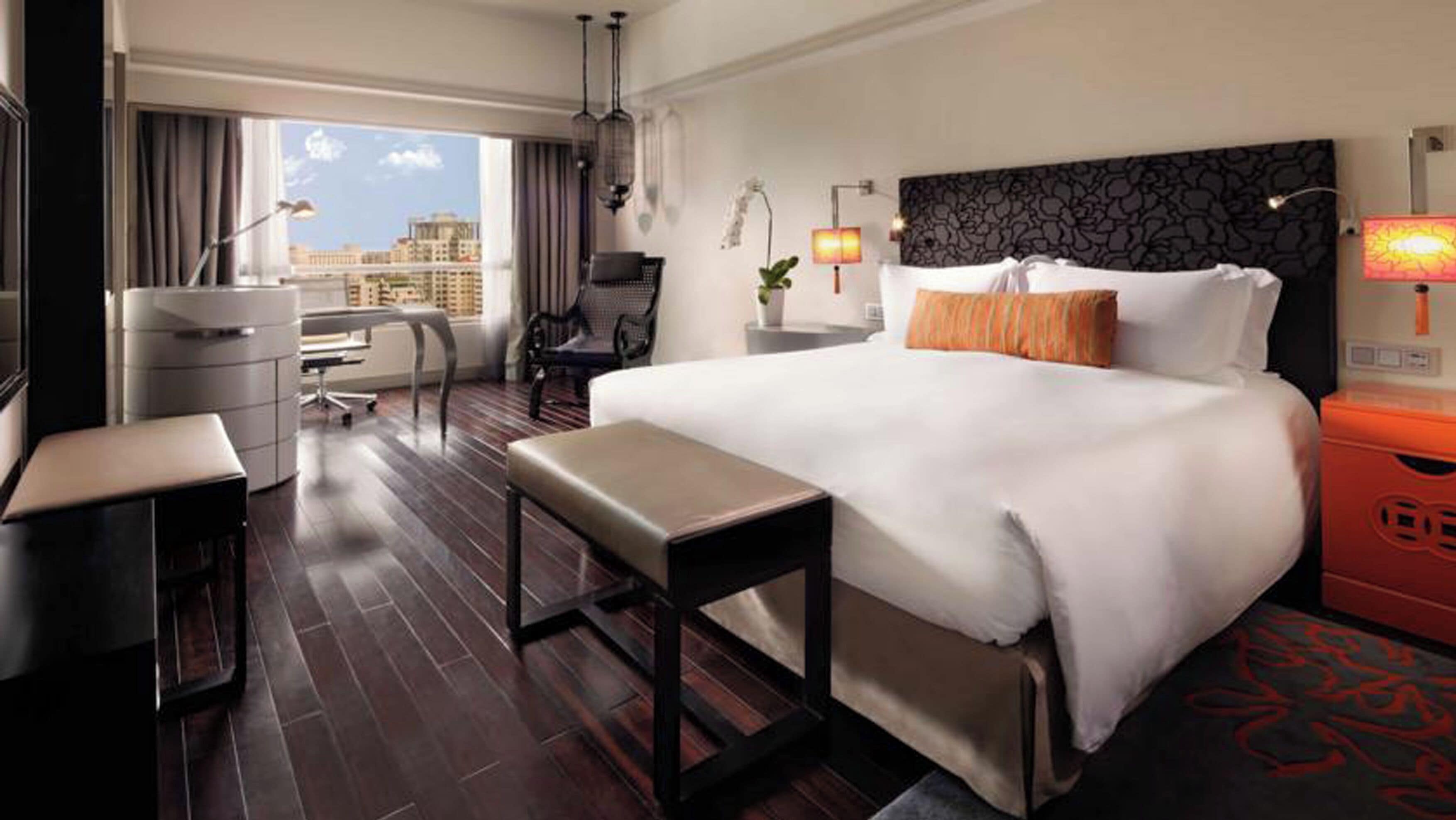 Habitación de hotel con una cama grande, un escritorio, una silla, una mesita y vistas a la ciudad.