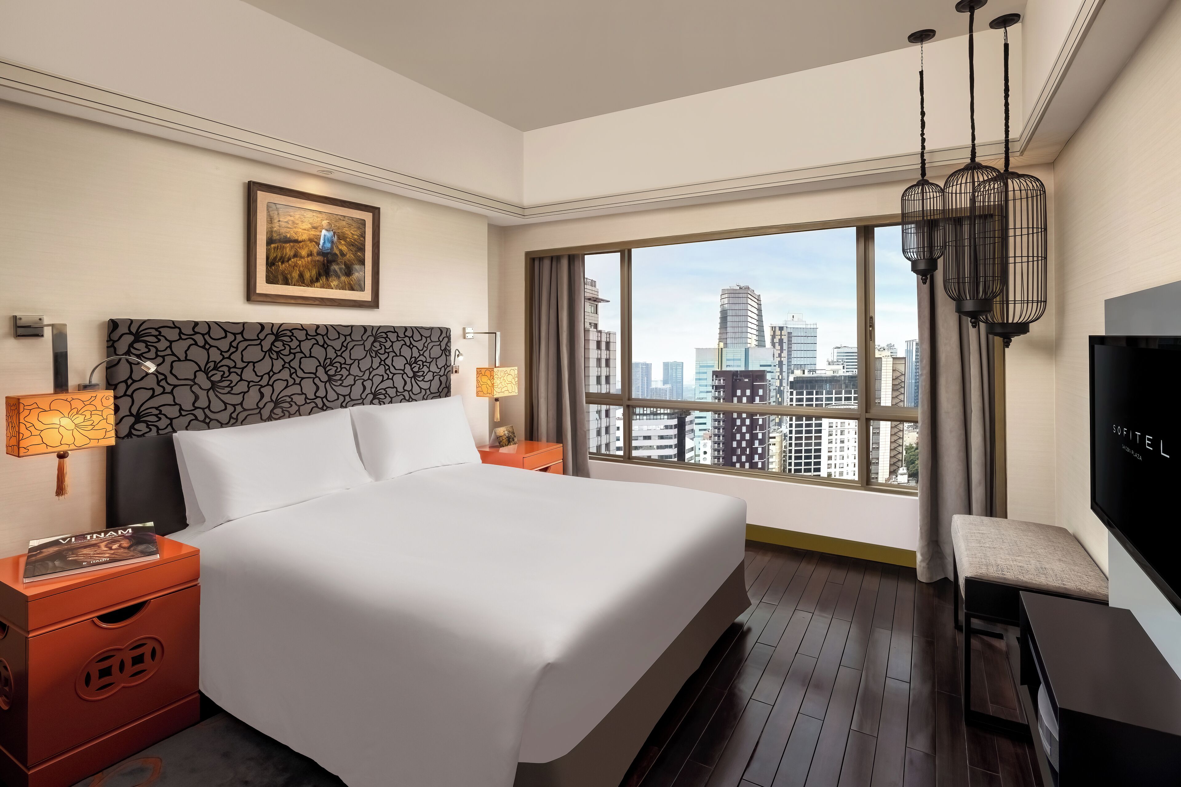 Ein Hotelzimmer mit einem großen Bett, einem Fernseher, einem Schreibtisch und Blick auf die Stadt durch große Fenster.
