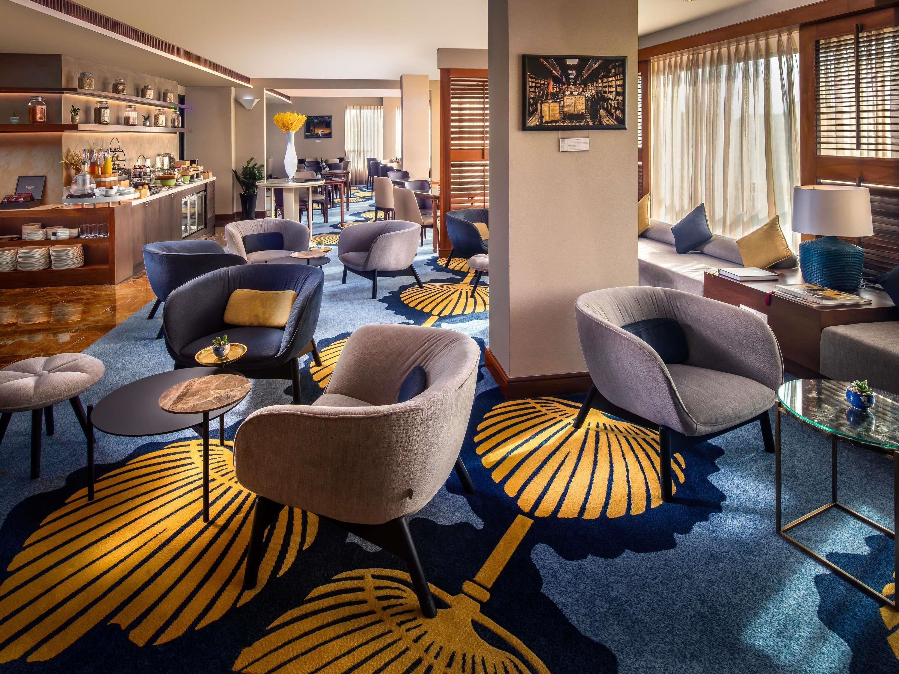 A hotel lobby with seating areas, a reception desk, and a view of the dining area.