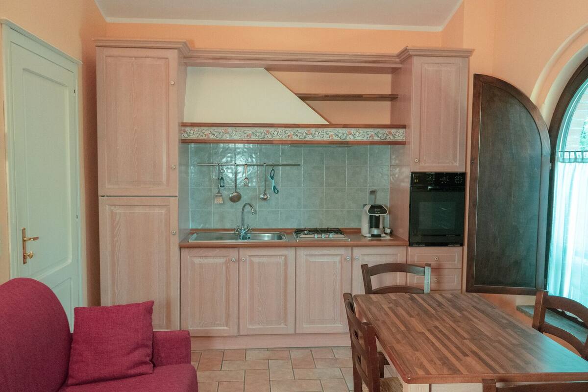 A compact kitchen with a sink, stove, and refrigerator. There is a dining table with chairs and a red sofa in the living area.
