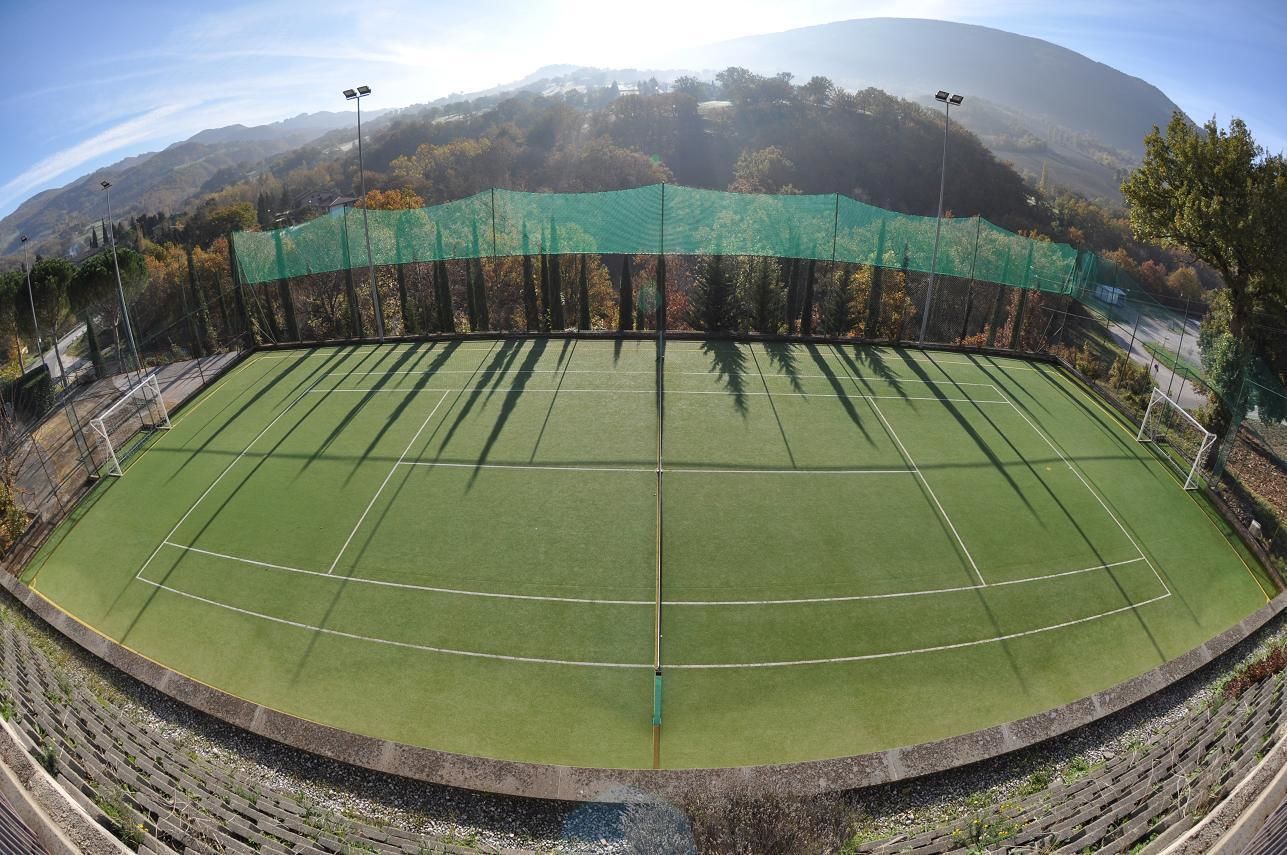 A tennis court with a net, surrounded by a green fence and trees.