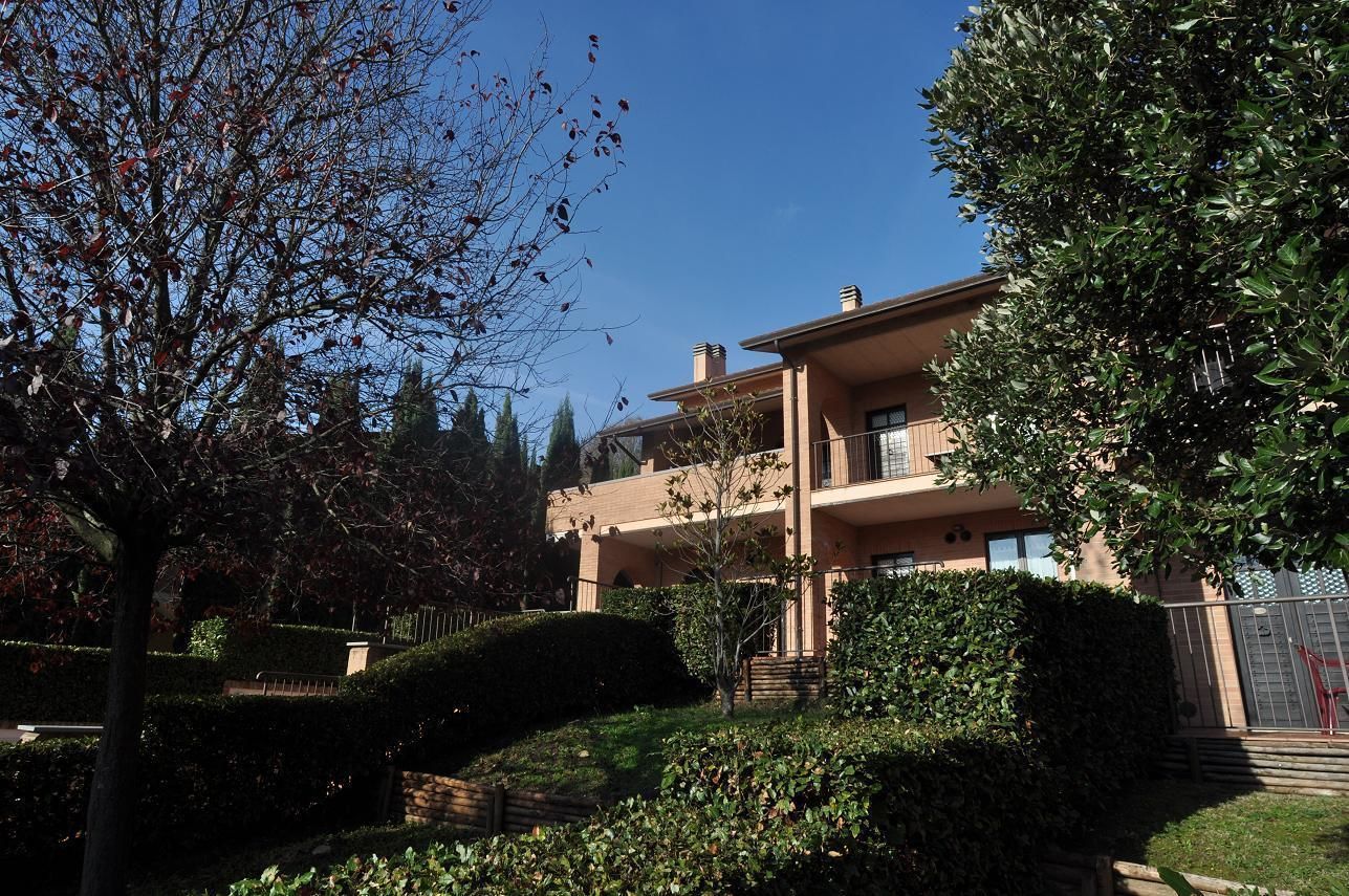 A two-story building with a balcony on the second floor, surrounded by well-maintained hedges and trees.