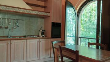 A kitchen with a dining area, a coffee maker, and a view of trees through a large window.