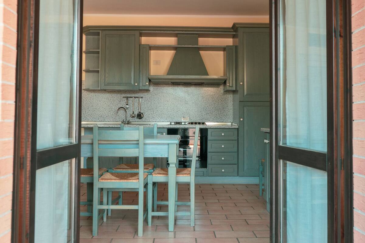 A compact kitchen with teal cabinetry, a small island with stools, and a tiled backsplash.