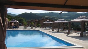 A swimming pool with lounge chairs and umbrellas, surrounded by buildings and a mountainous landscape. - Carpediem Assisi Living Club (Assisi)