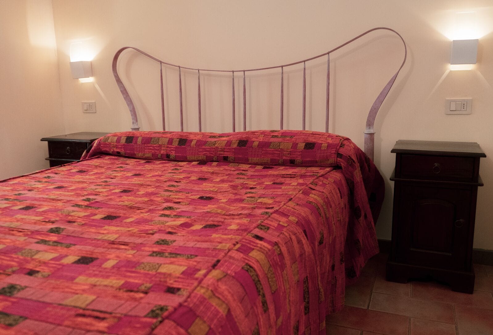 Una cama con colcha, dos mesitas de noche y luces fijadas en la pared.
