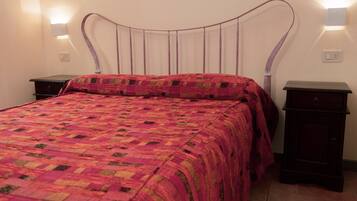 Una cama con colcha, dos mesitas de noche y luces fijadas en la pared.