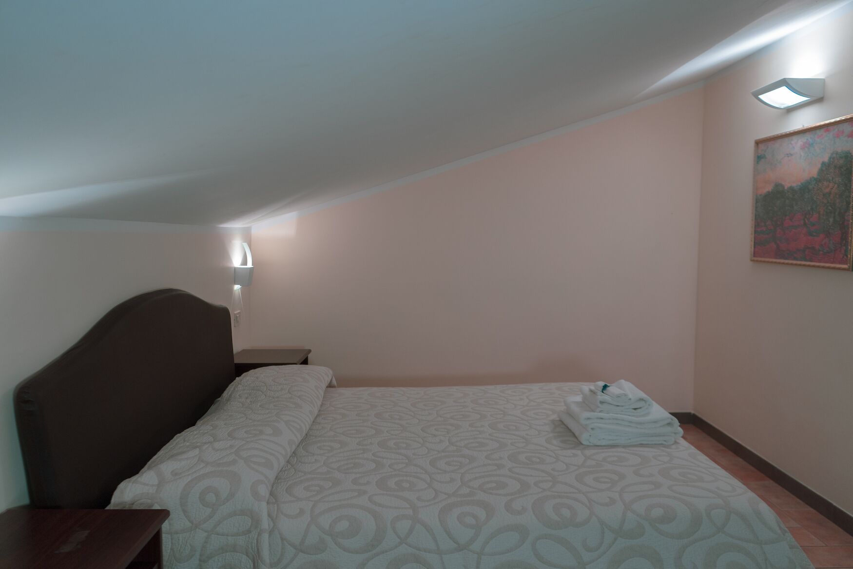 Ein Schlafzimmer mit einem Bett, einem Nachttisch, einer Wandleuchte und einem Bild an der Wand.