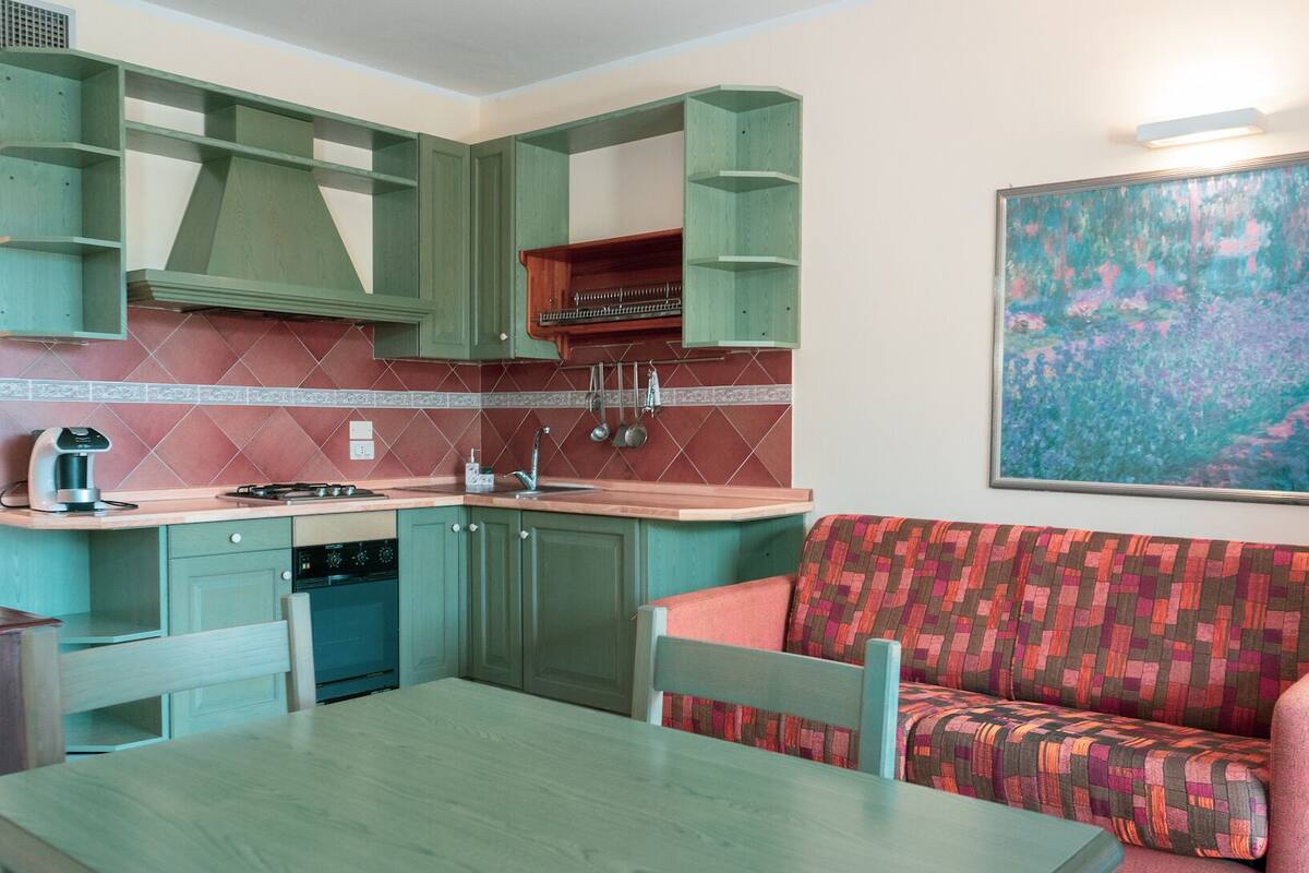 A compact kitchen with green cabinets, a dining table, and a sofa.