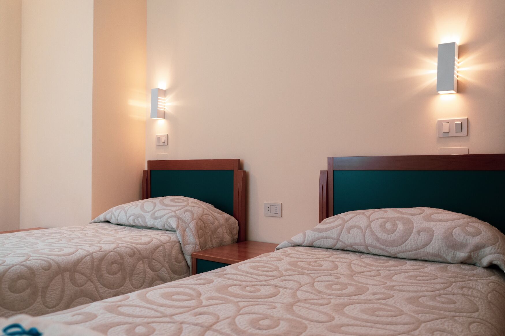 Two single beds with headboards, a nightstand, and wall-mounted light fixtures in a room.