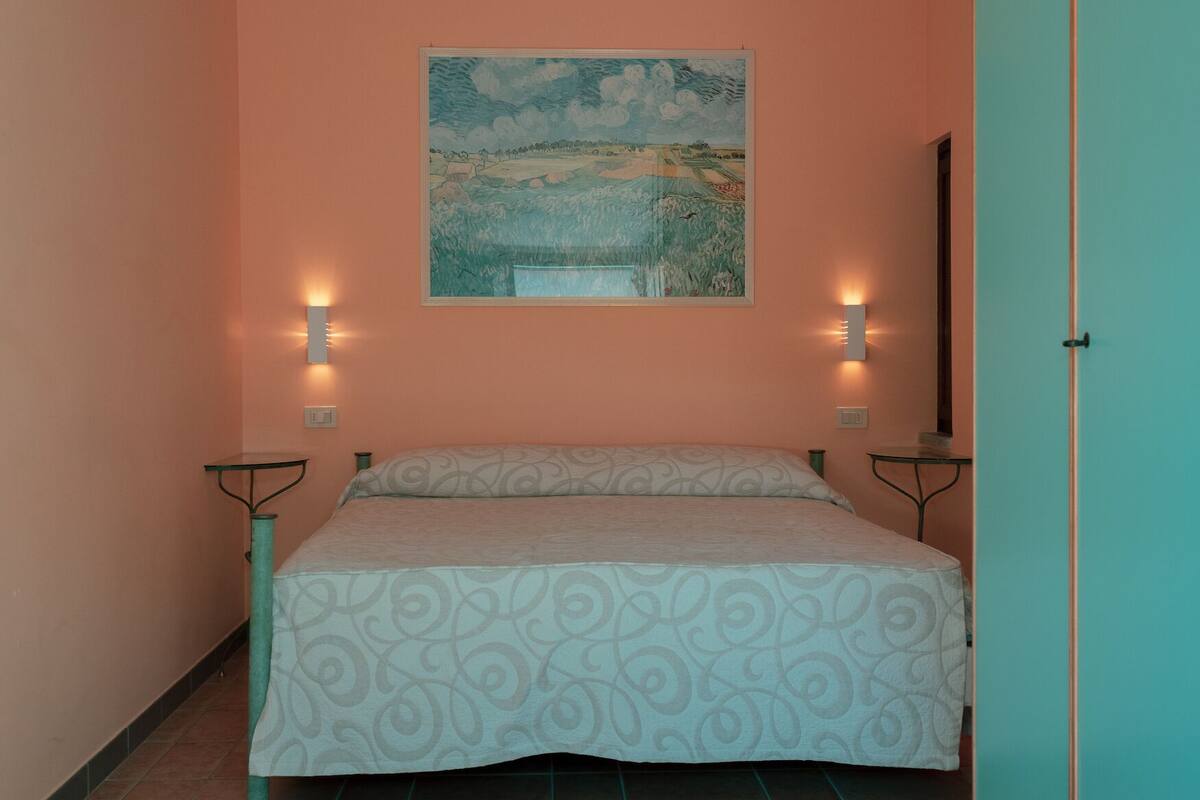 A bedroom with a bed, two bedside tables, a wall-mounted painting, and two wall-mounted lights.