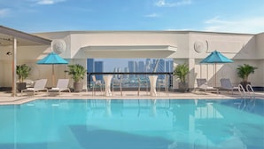 A rooftop pool with lounge chairs and umbrellas, a clear sky, and a city skyline view. - Renaissance Riverside Hotel Saigon (Ho Chi Minh City)