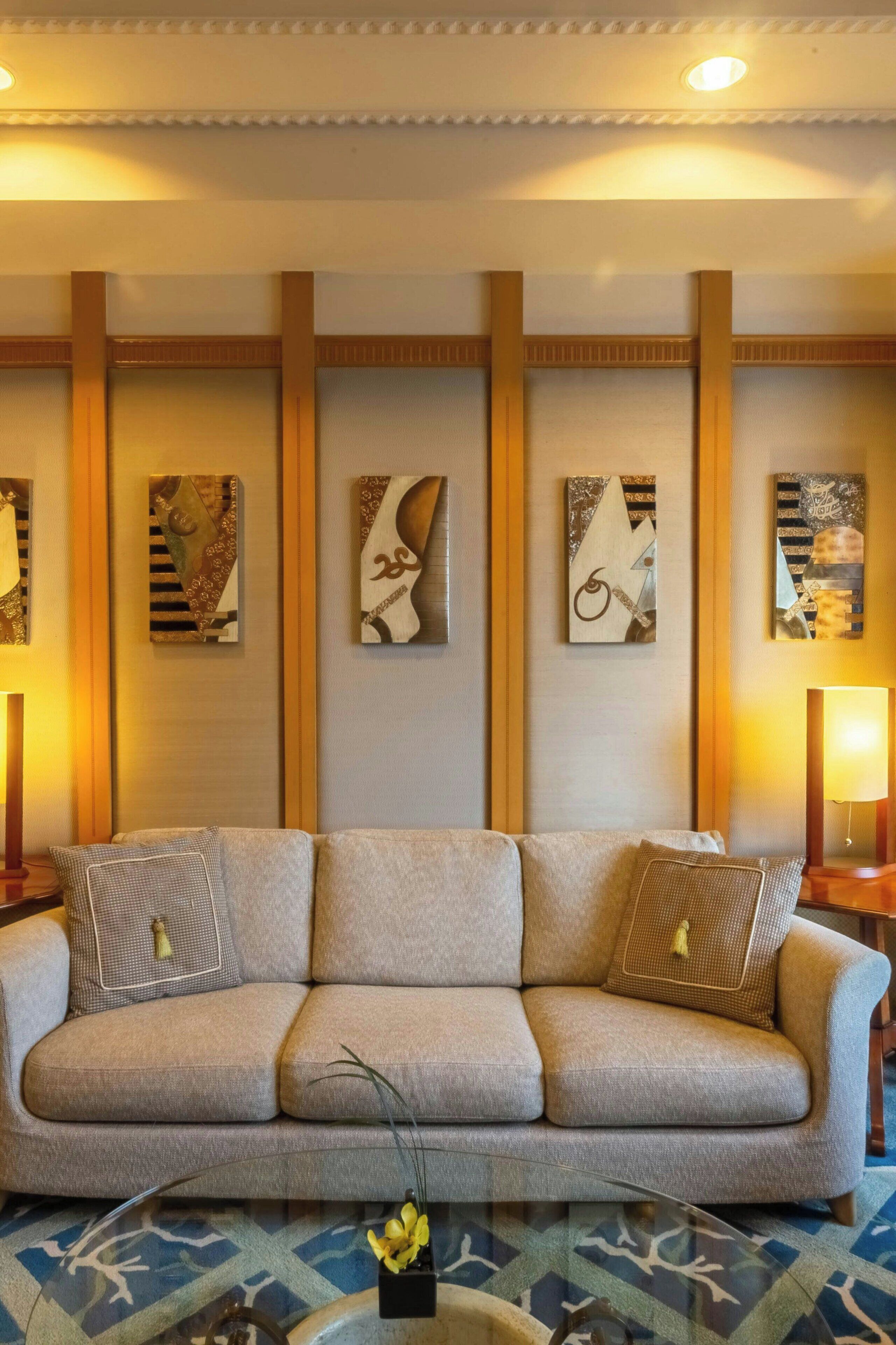 A modern living room with a beige sofa, abstract wall art, and a glass coffee table with a vase.
