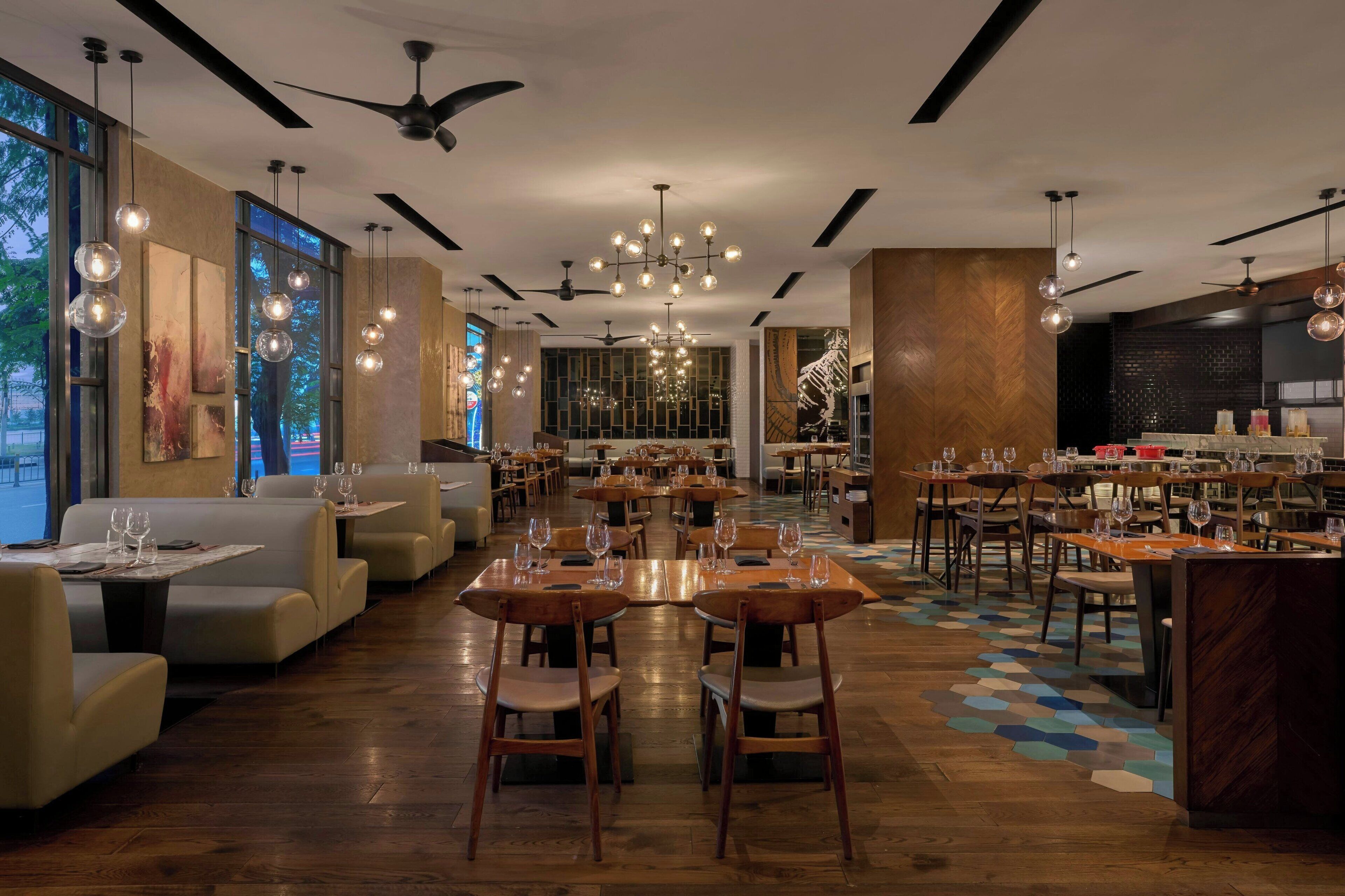 A restaurant with multiple dining areas, ceiling fans, hanging light fixtures, and large windows.