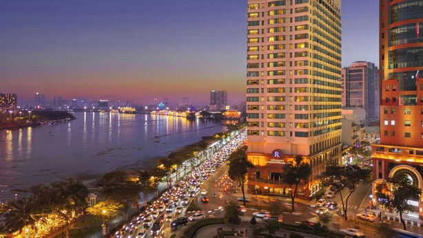 A high-rise hotel with multiple floors, a river in the background, and a busy street with cars. - Renaissance Riverside Hotel Saigon (Ho Chi Minh City)