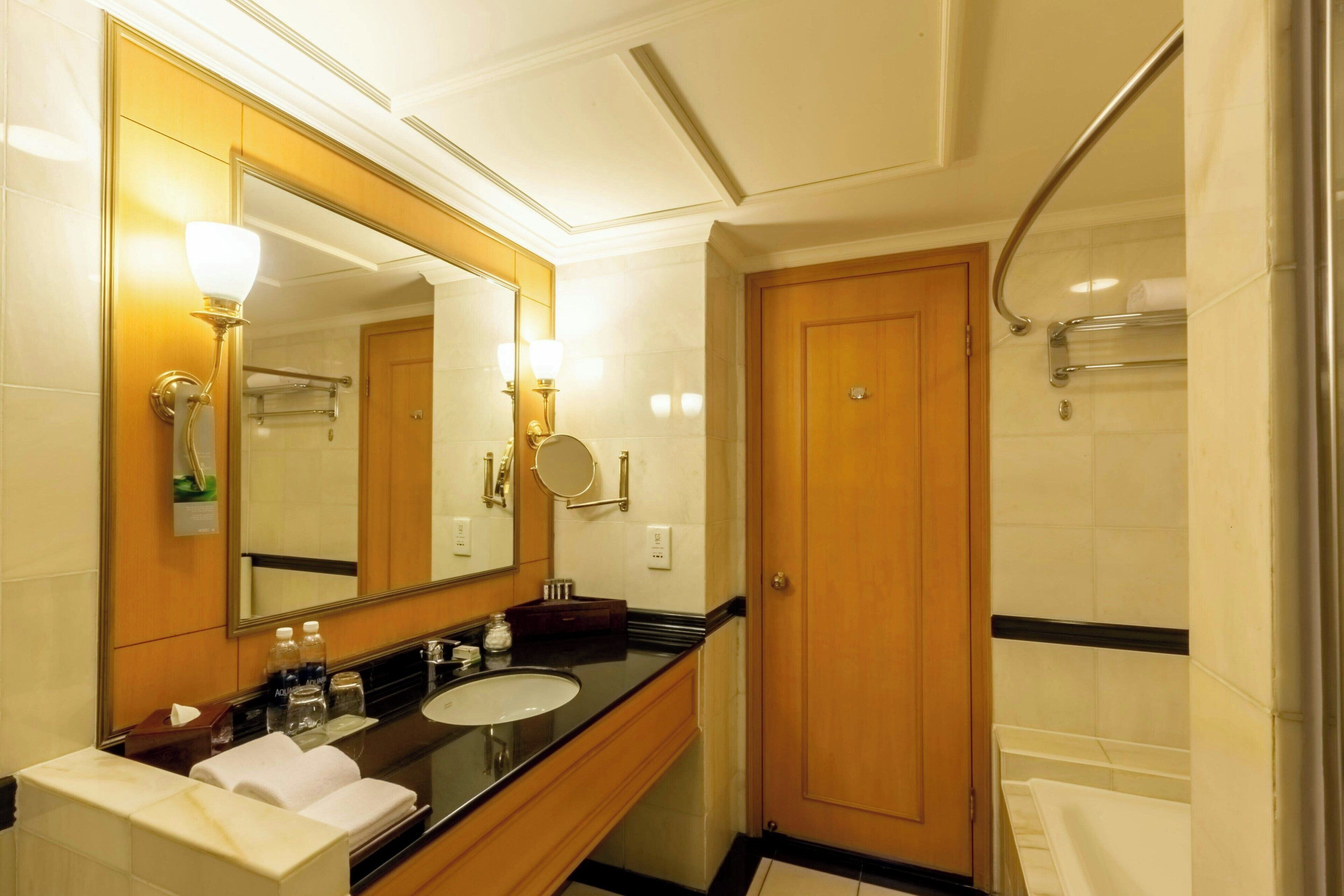 Un bany d'hotel amb un mirall gran, un lavabo, un moble de tocador i una zona de dutxa.