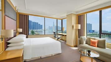 A hotel room with a large bed, a sofa, a desk, and a view of a cityscape.
