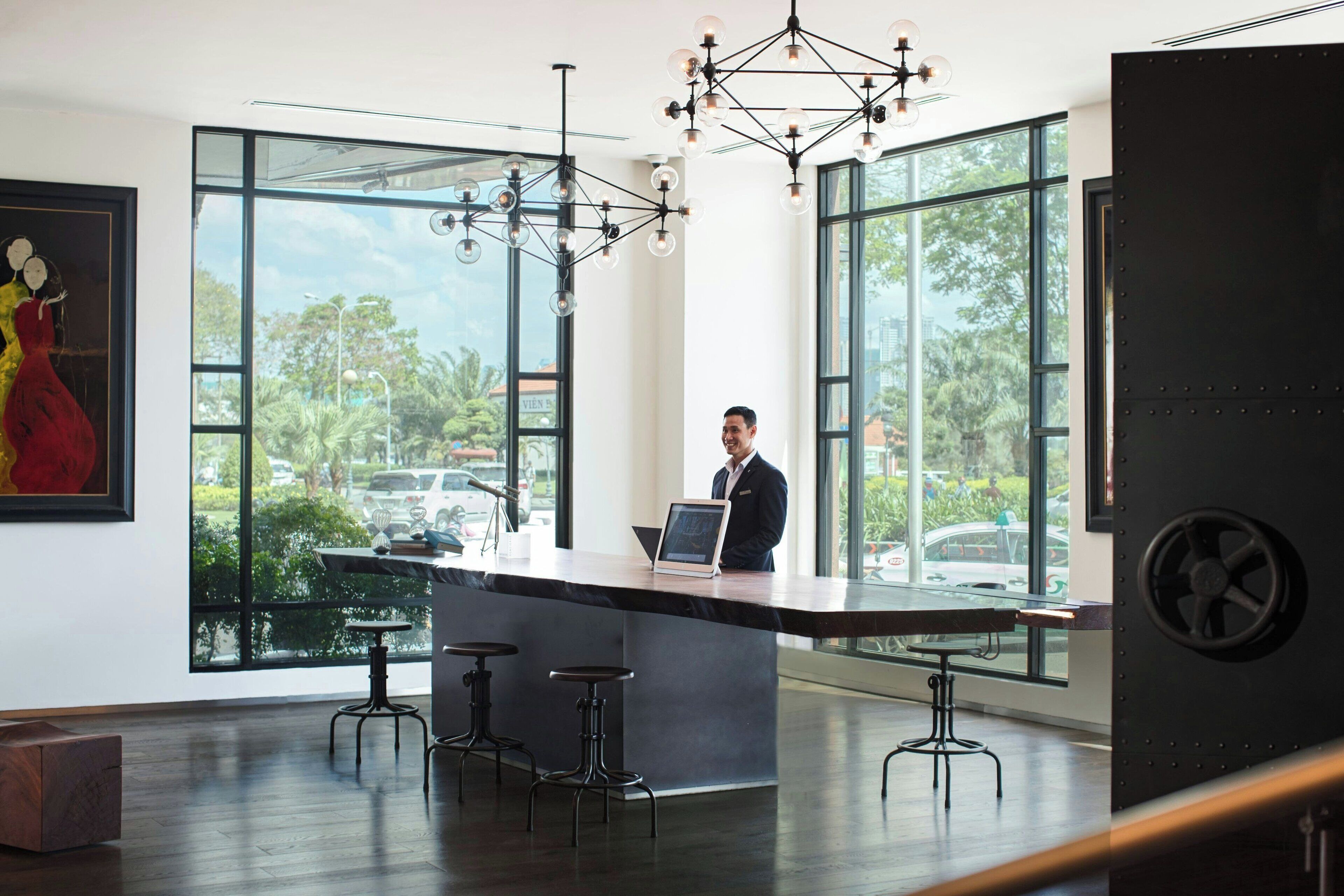 A modern bar area with a large window, a bartender, and a unique chandelier.