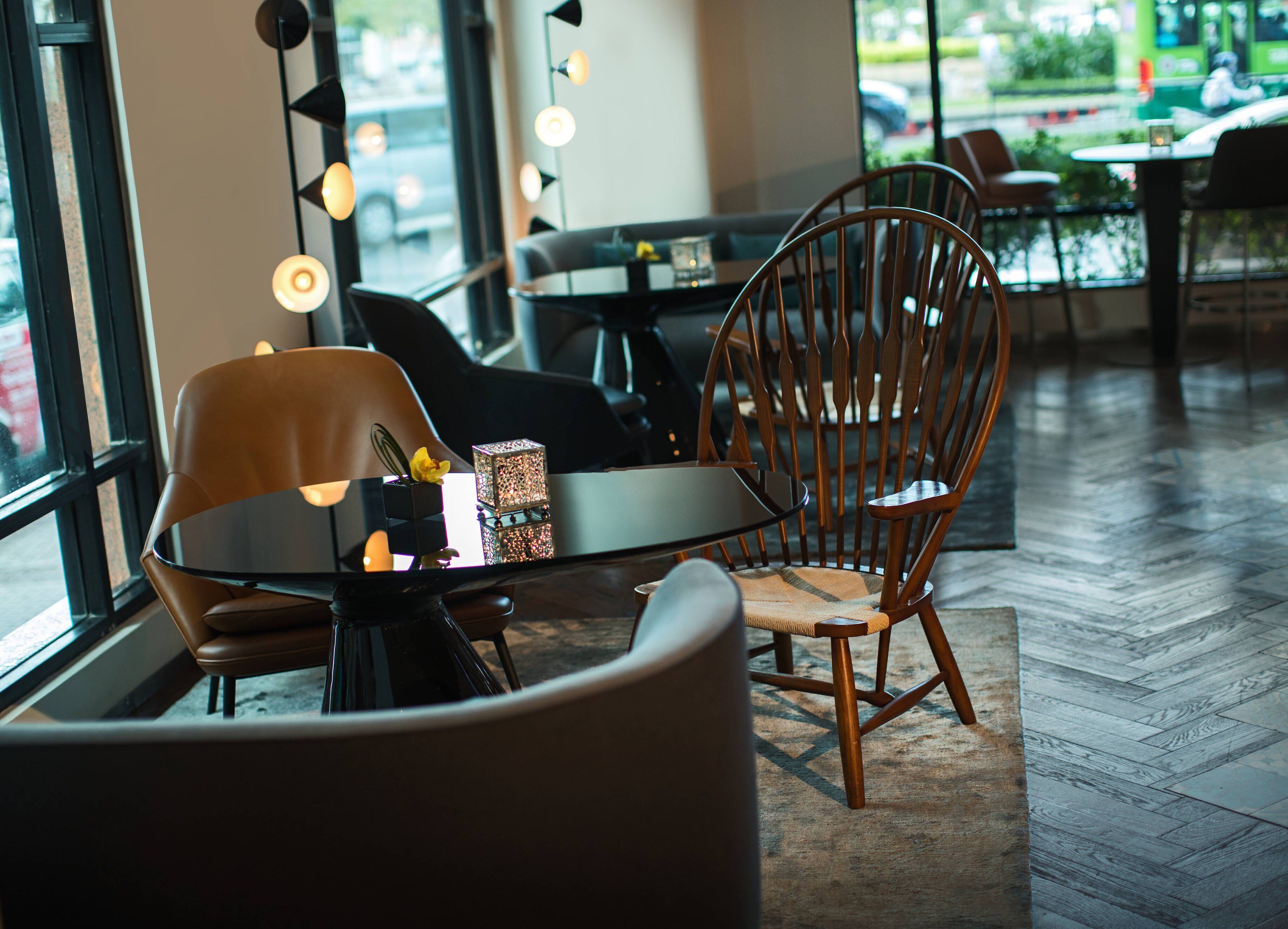 L'intérieur d'un café moderne, avec une chaise en bois, une table ronde et une vue sur la rue grâce à de grandes fenêtres.