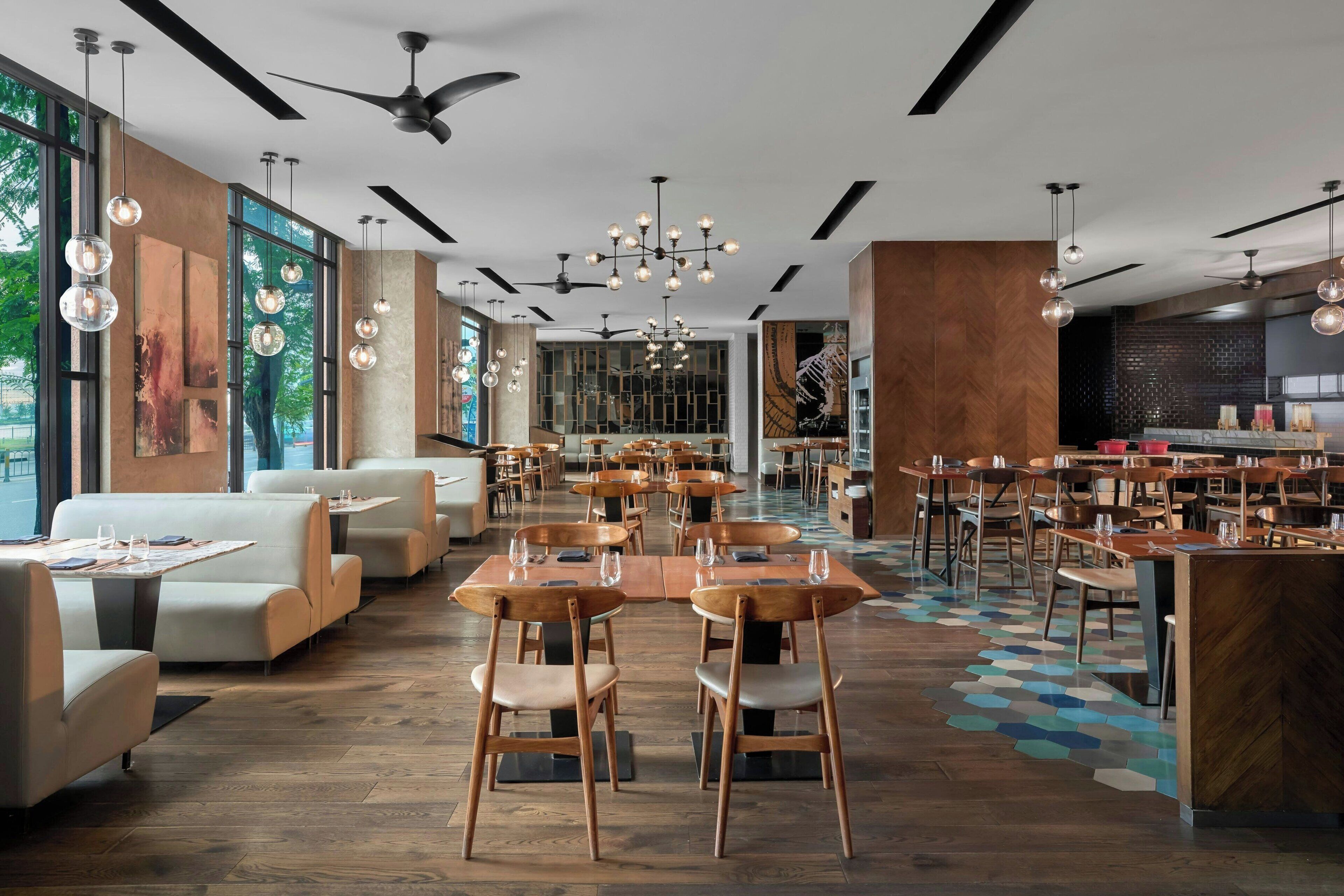 A modern restaurant with high ceilings, pendant lighting, and a mix of seating arrangements including tables and booths.