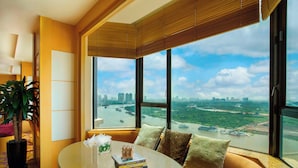 A modern living room with a glass table, a sofa with cushions, a potted plant, and a large window offering a city view. - Renaissance Riverside Hotel Saigon (Ho Chi Minh City)