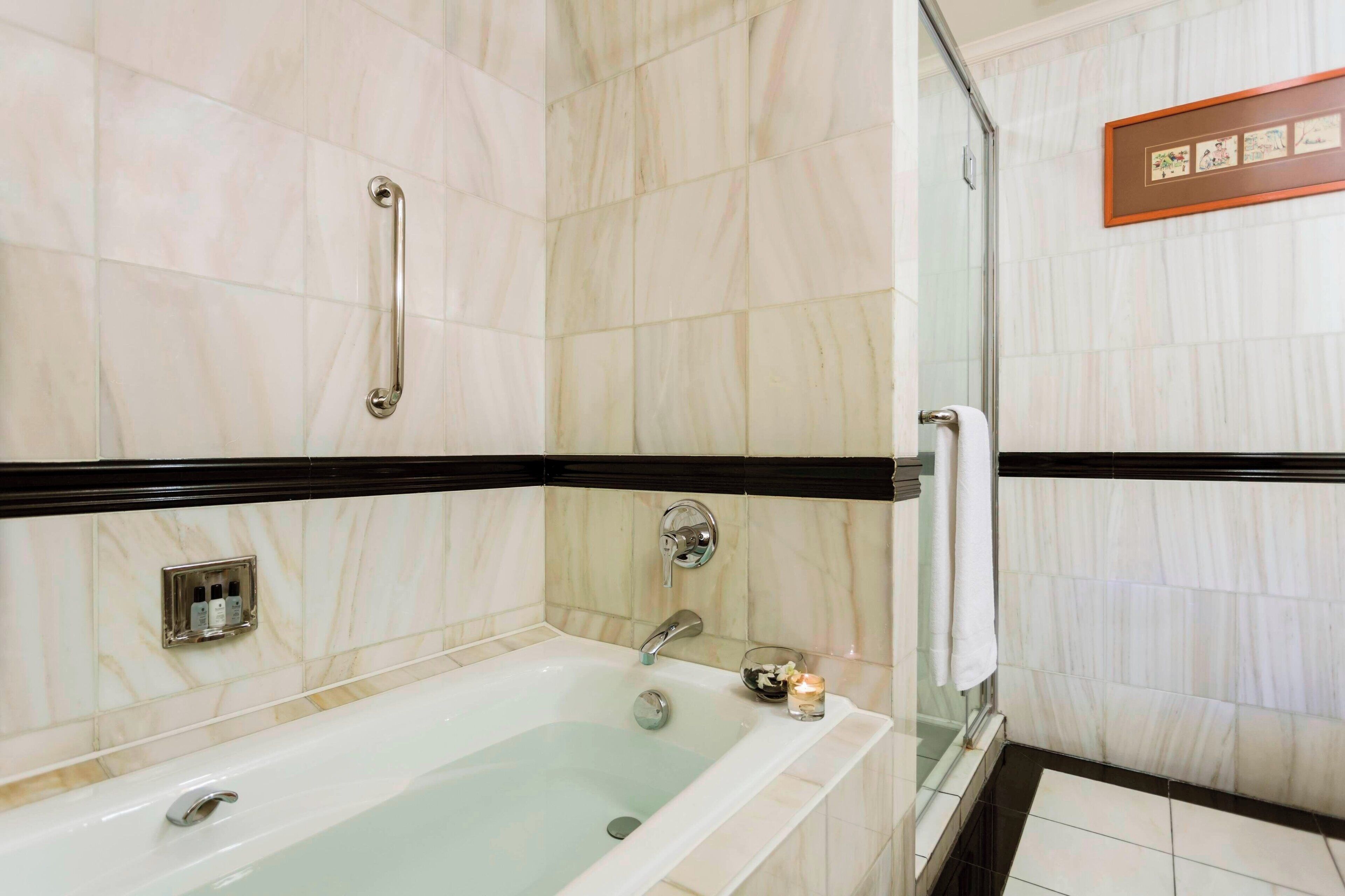 Un baño con bañera, barra de apoyo, toallero y un cuadro en la pared.