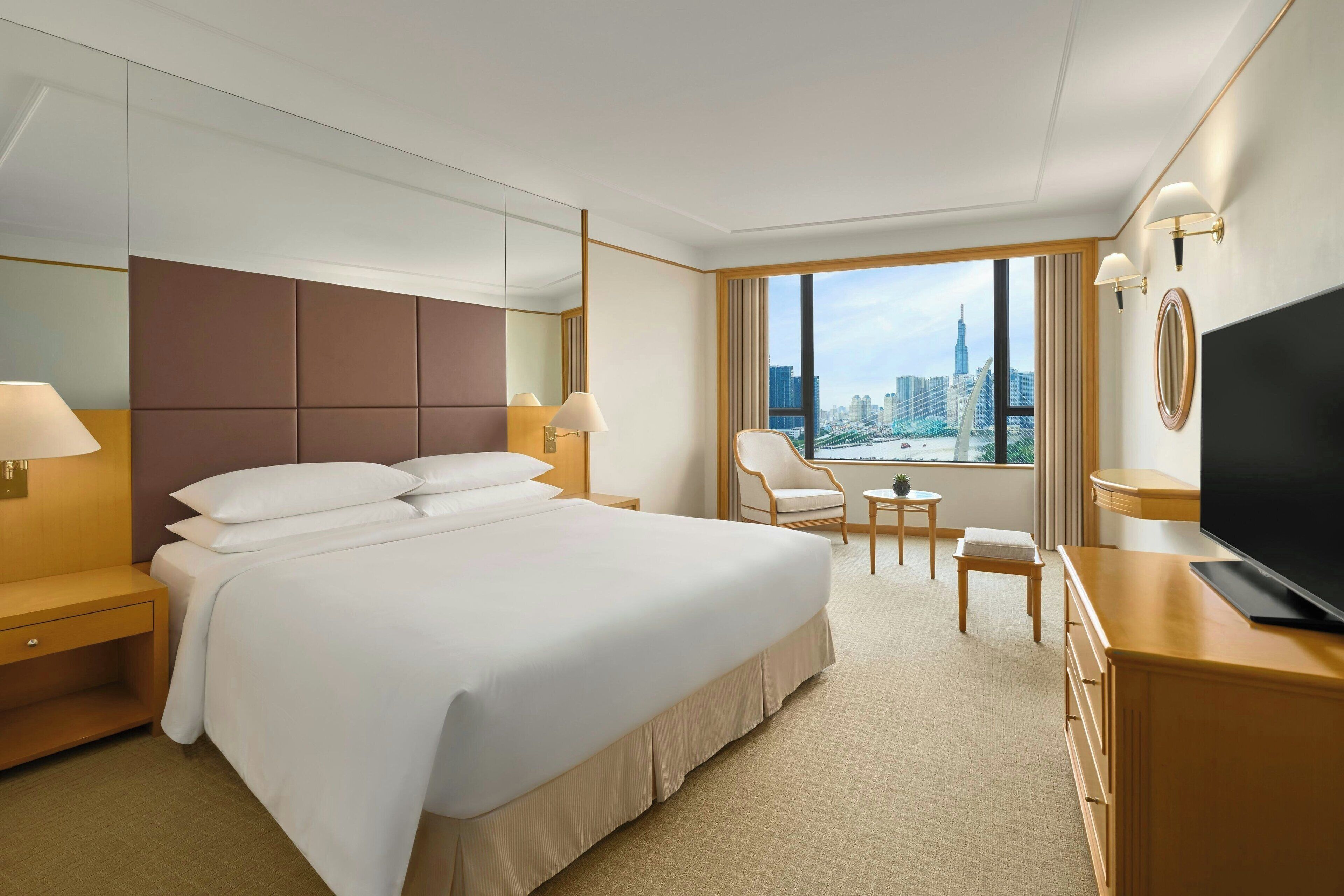 Habitación de hotel con una cama grande, televisión, escritorio, silla y vistas a la ciudad.