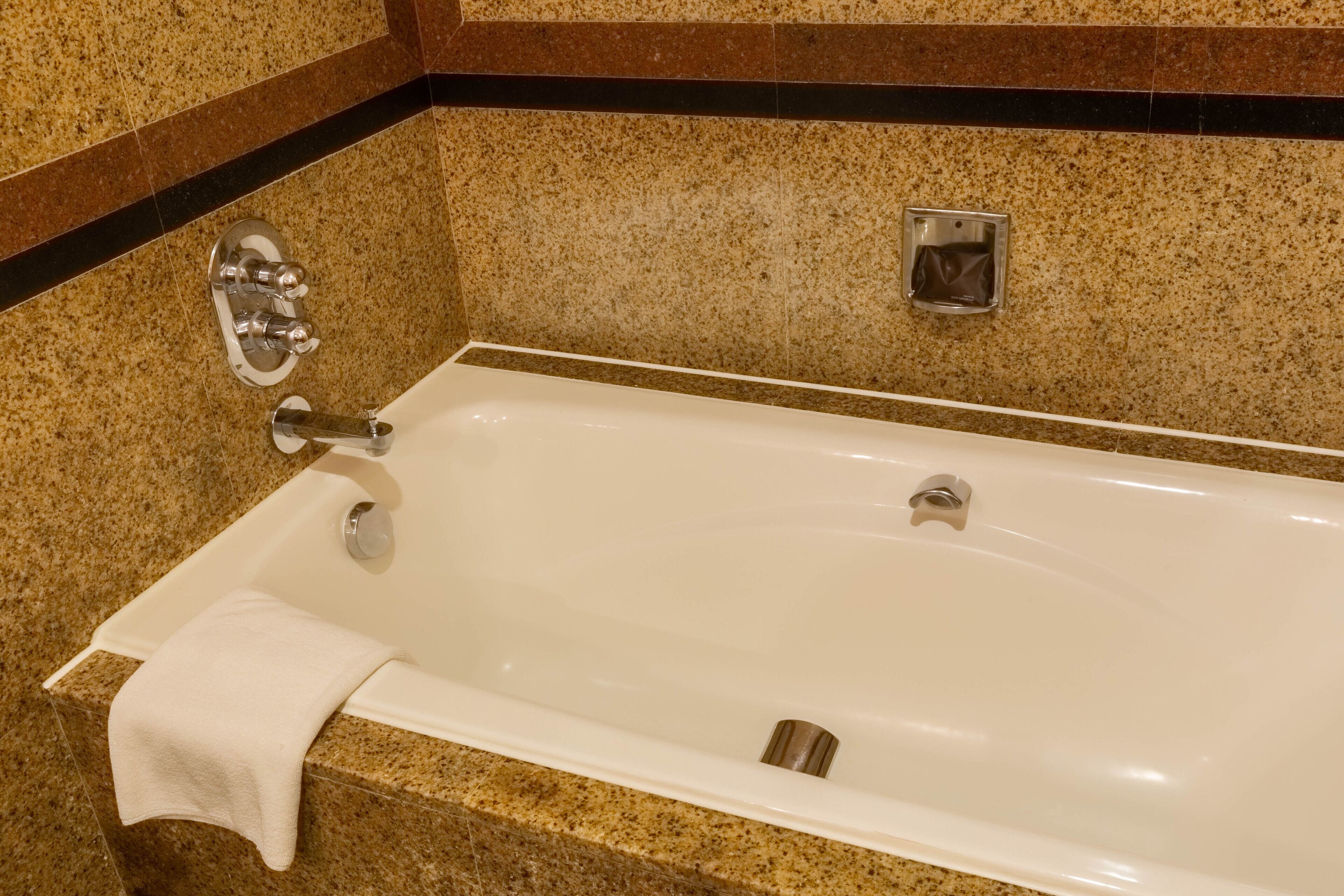 Una bañera con una toalla, un cabezal de ducha y un panel de control.