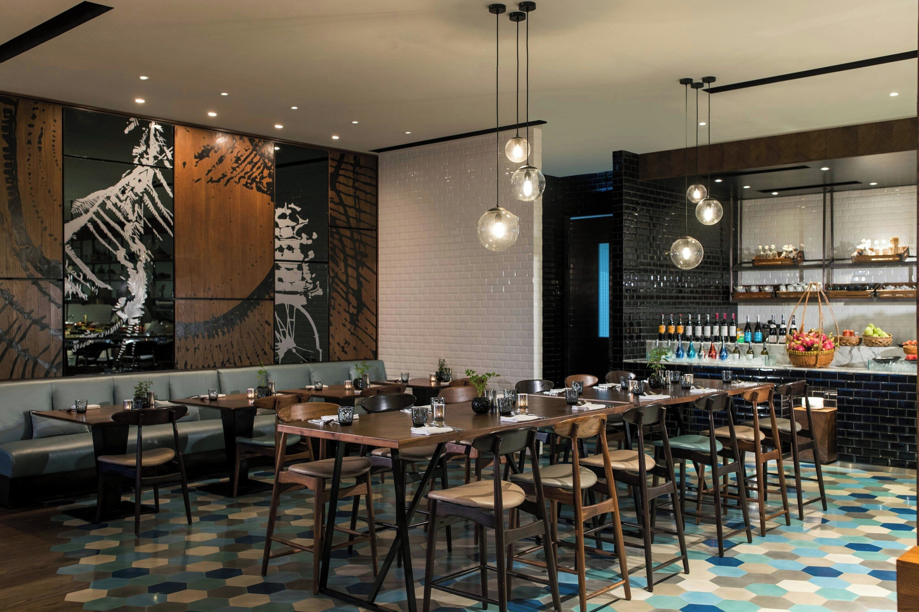 Un restaurante moderno con una larga mesa común, área de bar y un gran mural en la pared.