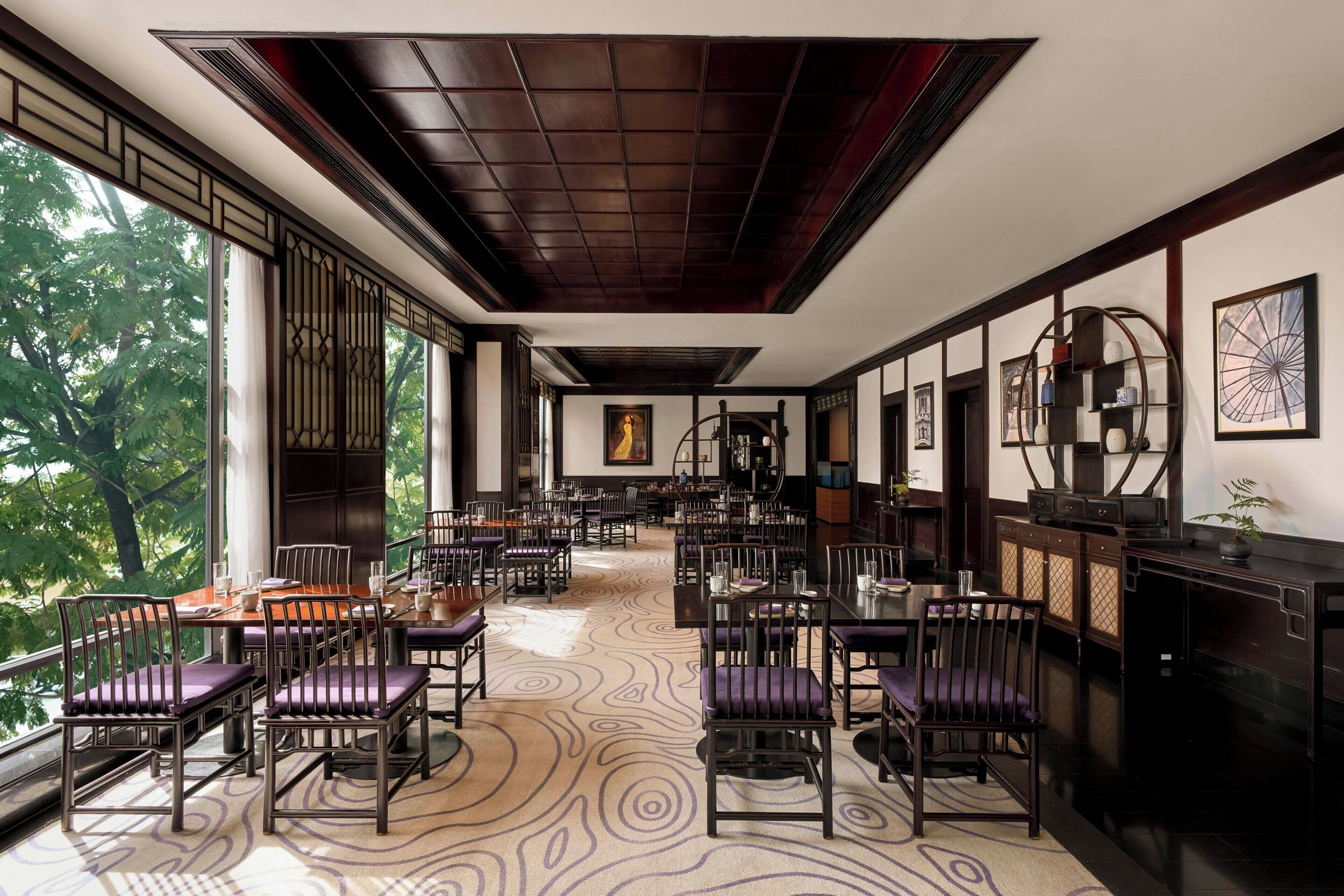 A spacious dining area with high ceilings, large windows, and a patterned carpet.