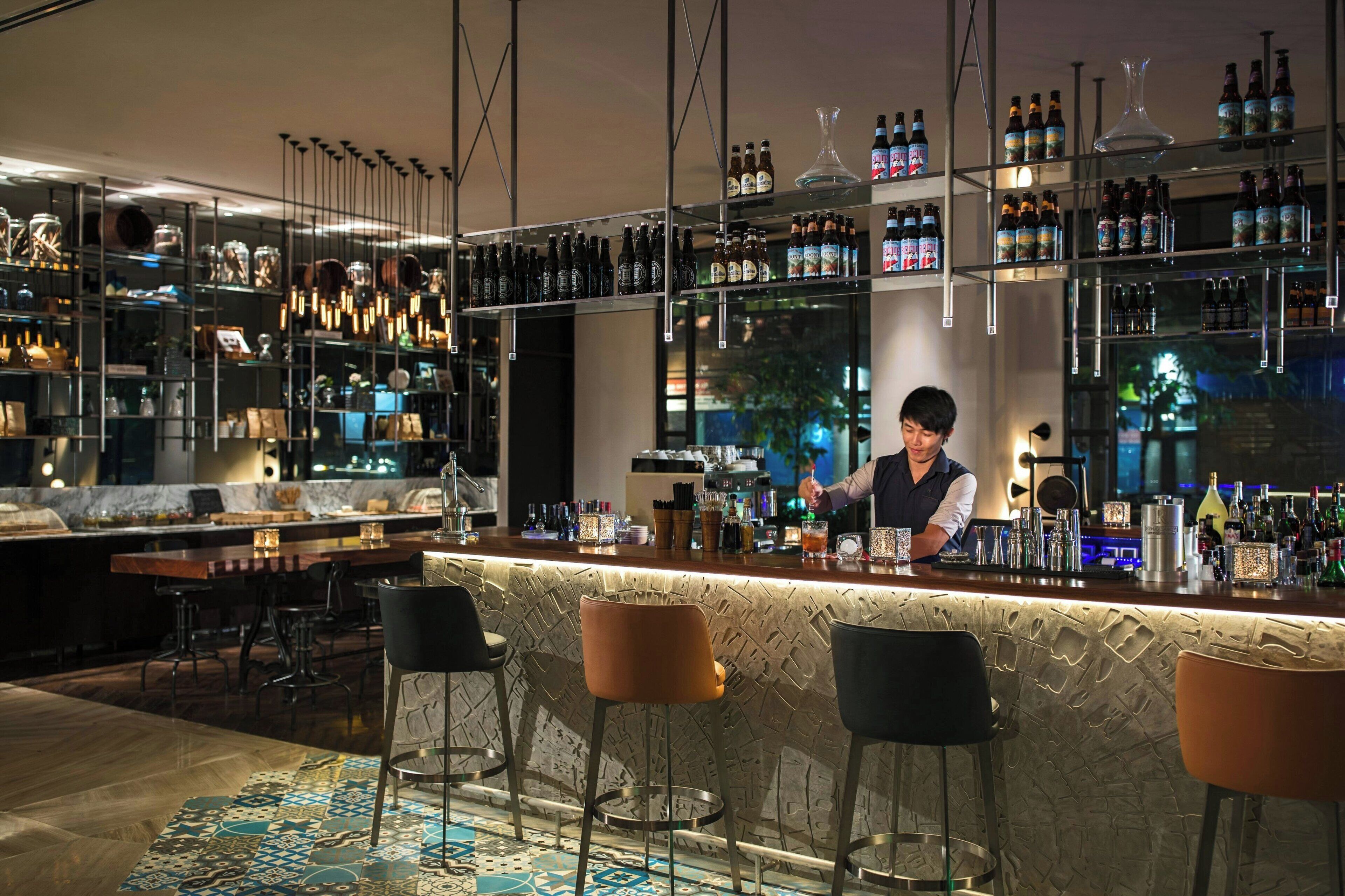 A bar area with a bartender, bar stools, shelves with bottles, and a patterned floor.