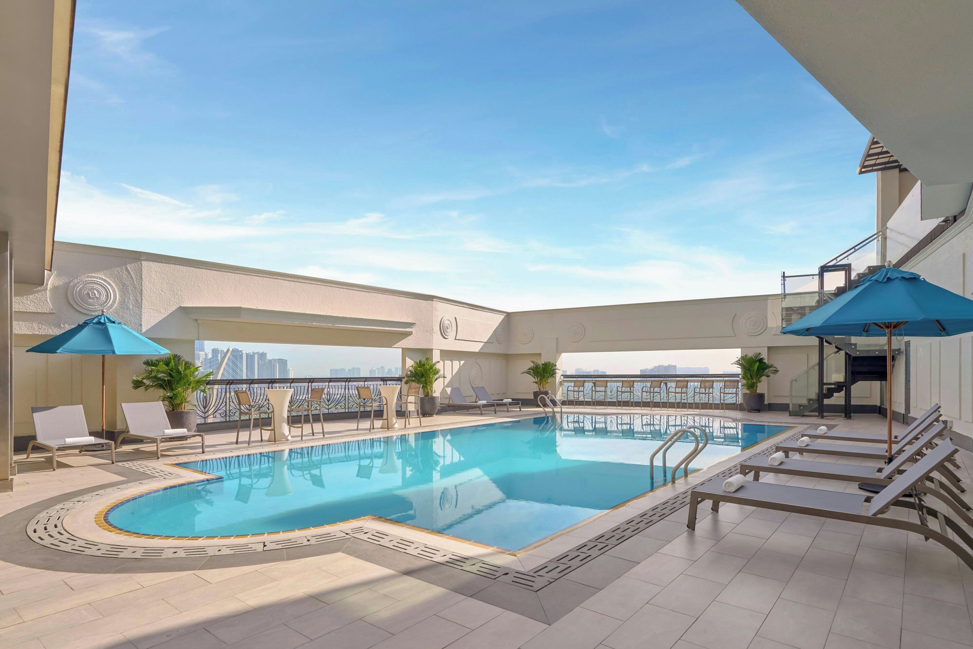 A rooftop pool with lounge chairs and umbrellas, surrounded by a high-rise cityscape.