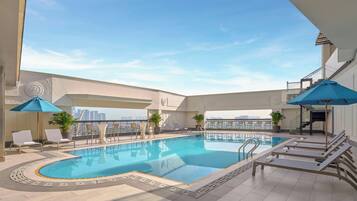 A rooftop pool with lounge chairs and umbrellas, surrounded by a high-rise cityscape.
