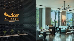 A modern restaurant interior with a black brick wall, a sign reading "Saigon Kitchen," and a dining area with tables and chairs. - Renaissance Riverside Hotel Saigon (Ho Chi Minh City)