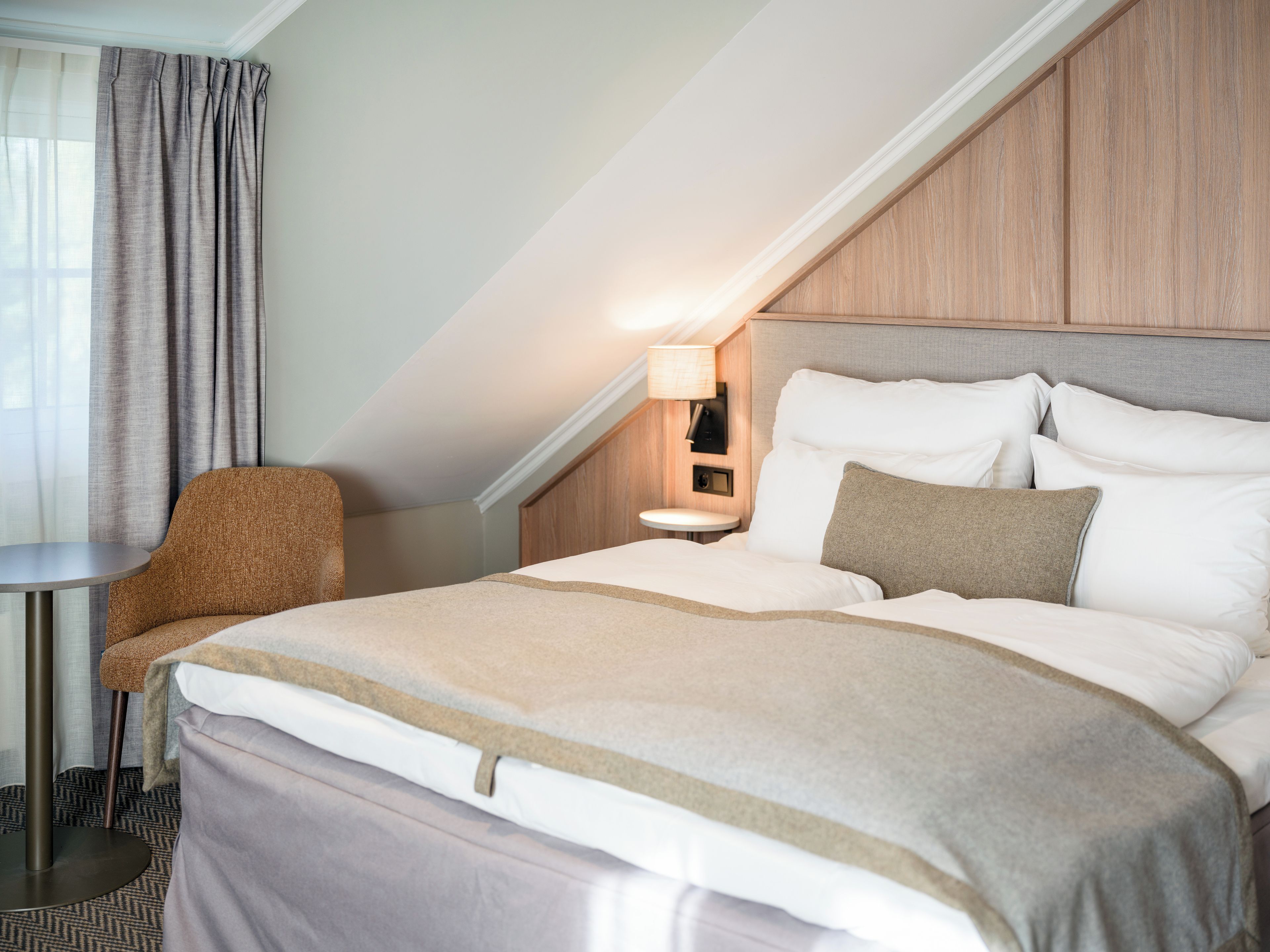 A hotel room with a bed, a nightstand, a lamp, a chair, and a view of the outdoors.